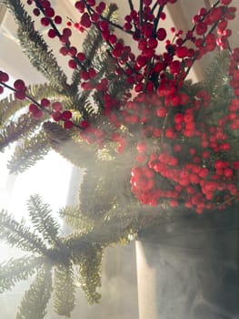 a bouquet of branches with red berries and fir branches in smoke in sunny weather, the rays of the sun through the branches. High quality photo