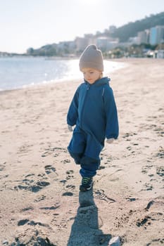 Little girl walks along the sandy beach, looking at her feet. High quality photo