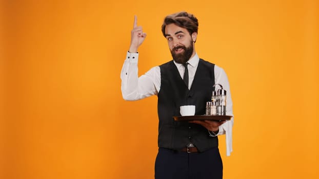 Qualified worker in studio having new idea, standing with food tray in hand and raising index finger upwards. Competent butler carrying cutlery and drink to serve people, restaurant sector.