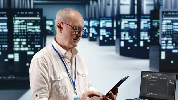 Meticulous computer scientist in data center, solving tasks on tablet while running scripts on laptop terminal. Precise admin amidst servers, accessing databases and manipulating lines of code