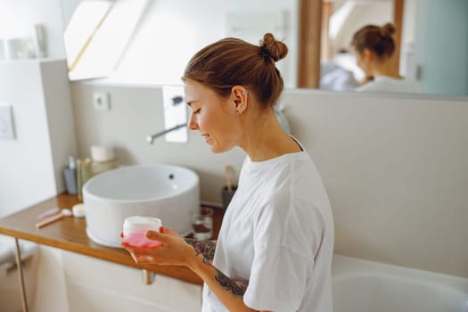 Young woman holding jar with skincare cream in hands. Home beauty routine