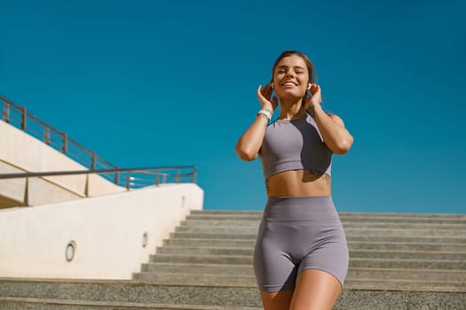 Smiling woman in sportswear have a rest after workout outside standing on stairs background