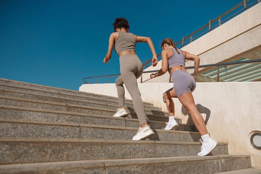 Two active female athlete friends in sportswear running on steps outdoors on a sunny day