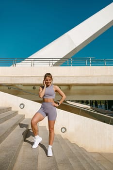 Smiling woman in sportswear have rest after workout outside standing on stairs background