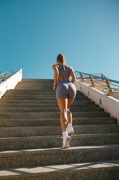 Back view of active female athlete in sportswear running on steps outdoors on a sunny day