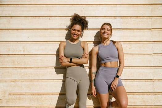 Two young female sportswomen have a rest after morning jogging outdoors and looks camera