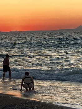 beautiful girl stands in the sea on the background of wonderful red sunset in Creta, Greece, 02 August 2023. young woman in black swimsuit staying by the waves of the sea water. Silhouette of a girl on the beach at sunset High quality photo