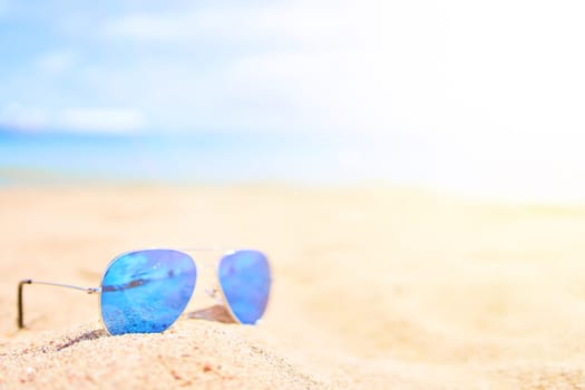 Sunglasses on the sand with ocean and sky on background