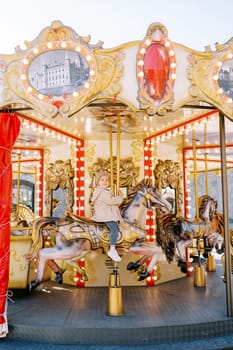 Little smiling girl rides a toy horse on a colorful carousel in a square. High quality photo