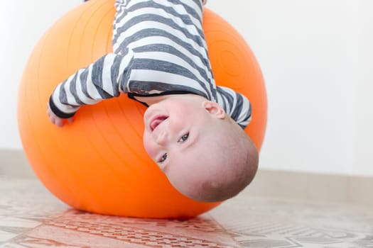 Smiling little boy lying on a fitball upside down. Horizontal studio shot.