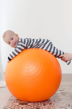 A little boy with tongue out lying on a fitball. Vertical studio shot.