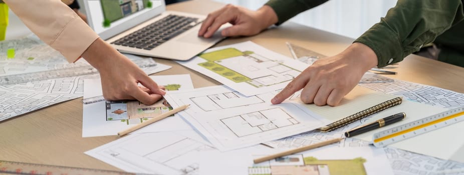 Professional architect shows mistake structure in blueprint while analysis and comparison with picture in laptop on table with blueprint and architectural equipment. Cropped image. Delineation.