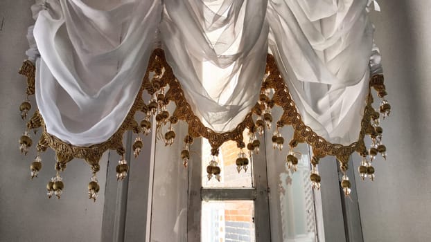 Elegant Window Drapes With Tassel Trim Overlooking a Sunny Day. White sheer curtains with decorative tassels framing a clear view of a blue sky. Background, texture, pattern, frame