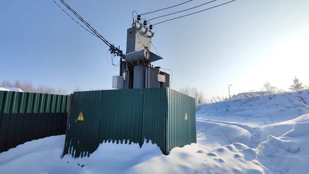 Winter Scene of a Transformer Electric Booth in Russia. Snow-covered ground surrounding a transformer booth with cables against clear sky