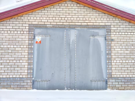 closed iron gate on a gray brick wall of a garage outside in white snow