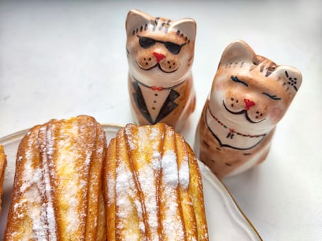 Delectable Dessert Pastries With Charming Porcelain Cat Figurines. Piped cakes sprinkled with sugar beside whimsical cat ornaments