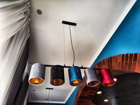 Modern Pendant Lights Hanging From White Ceiling in a Contemporary Room. Five colorful pendant lights illuminate a stylish room with a brick accent