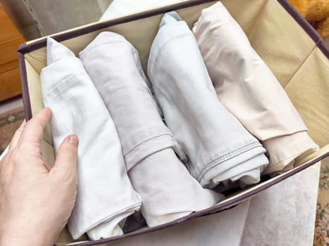 Organized Clothing Storage Using Konmari Folding Method. Neatly folded clothes arranged vertically in a storage box