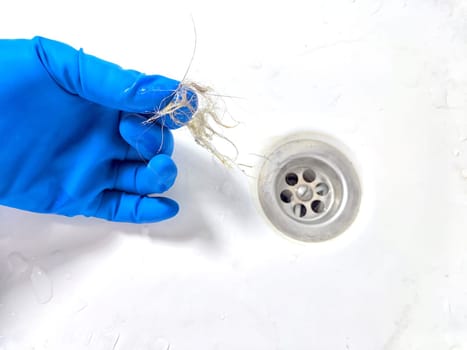 Removing Hair Clog From a Bathroom Sink Drain. Gloved hand extracting hair from sink
