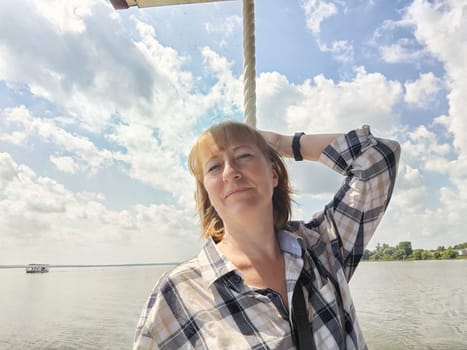 Happy cheerful middle aged woman taking selfie on nature outdoors and sun with water of lake or river on the background in summer day