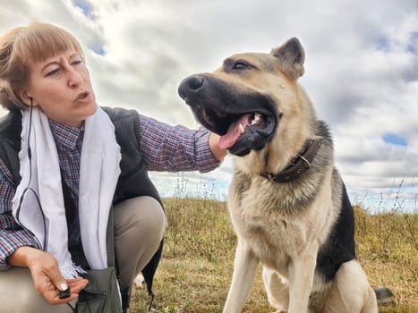 Adult girl with shepherd dog taking selfies in field. Middle aged woman and big shepherd dog on nature. Friendship, love, communication, fun, hugs
