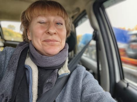 Funny cute blonde girl or a middle-aged woman driving a car in summer, autumn, spring day. A female driver on a solo trip