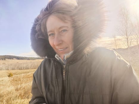Happy female blonde tourist in a warm jacket taking selfie with outside in cold summer, autumn or winter day. Middle aged woman having fun in nature trip