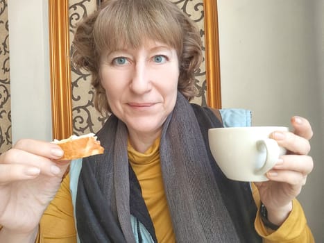 Mature Woman Enjoying Light Breakfast With Coffee by the Window. Woman in with morning coffee and bread. A blogger takes selfie while eating