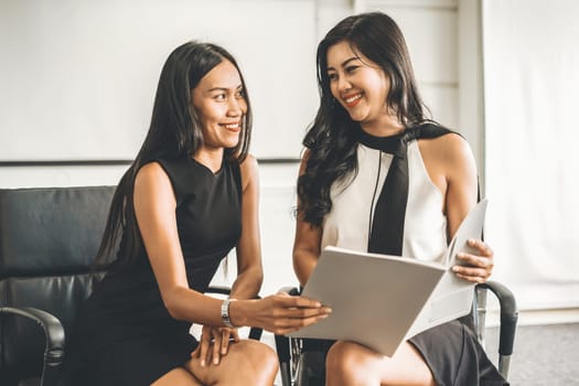 Two businesswomen discussing business while looking at financial data in their hands. They are sitting on the chairs in the office meeting room. uds