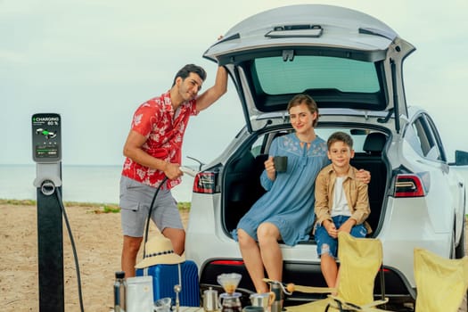Family vacation trip traveling by the beach with electric car, happy family recharge EV car, enjoying outdoor camping coffee. Seascape travel and eco-friendly car for clean environment. Perpetual