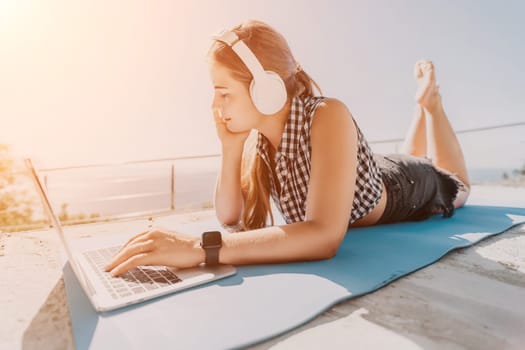 Digital nomad, Business woman working on laptop by the sea. Pretty lady typing on computer by the sea at sunset, makes a business transaction online from a distance. Freelance, remote work on vacation