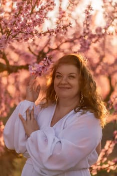 Woman blooming peach orchard. Against the backdrop of a picturesque peach orchard, a woman in a long white dress enjoys a peaceful walk in the park, surrounded by the beauty of nature