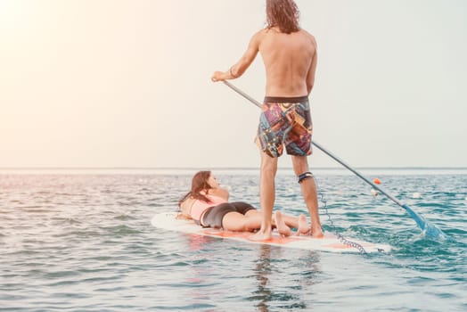 Sea woman and man on sup. Silhouette of happy young woman and man, surfing on SUP board, confident paddling through water surface. Idyllic sunset. Active lifestyle at sea or river