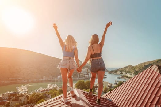 women standing on rooftop, enjoys town view and sea mountains. Peaceful rooftop relaxation. Below her, there is a town with several boats visible in the water. Rooftop vantage point