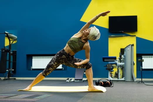 slender athletic woman in the gym is beautifully engaged in yoga exercises on a mat