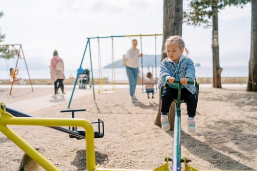 Little girl sits on a swing-balancer in the playground and looks down. High quality photo