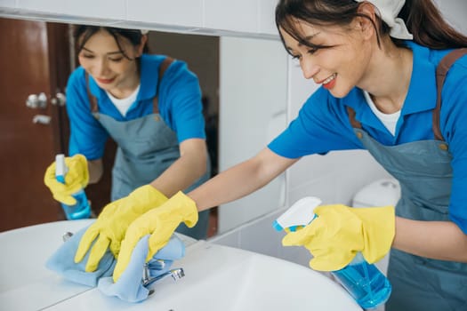 Maid with gloves scrubs limescale from bathroom sink and faucet applying spray detergent. Her occupation focuses on hygiene shiny fixtures and routine house care. spray cleaner