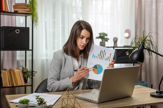 Young business woman working on laptop at office table talk on online communication video call with employee boss shows graphical analytics. Caucasian girl support services looks at webcam of computer