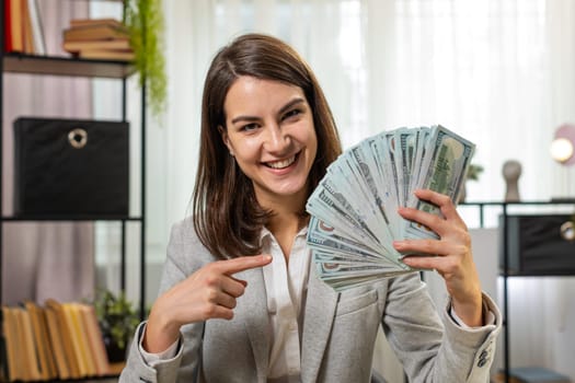Smiling businesswoman counting cash money dollar checking salary enjoy richness at modern workplace. Happy brunette freelancer girl calculating currency profit financial savings at home office desk.