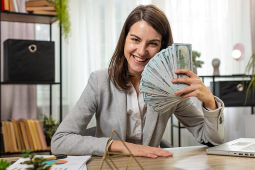 Smiling business woman counting cash money dollar checking salary enjoy richness at modern workplace. Happy brunette freelancer girl calculating currency profit financial savings at home office desk.