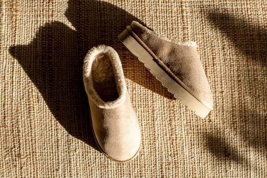 One pair of modern fashionable warm Uggs slippers on a high platform lie in the center on a woven jute rug on a winter day with shadows from the sun, flat lay close-up. Concept fashionable shoes.