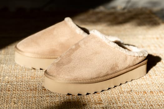 One pair of modern fashionable warm Uggs slippers on a high platform lie in the center on a woven jute rug on a tiled floor in the living room on a winter day with shadows from the sun, close-up side view. Fashionable shoes concept.