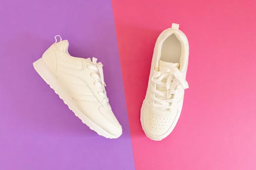 One modern fashionable white sneakers lie in the center on a lilac-pink background, flat lay close-up. Fashionable shoes concept.
