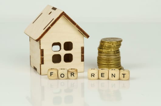 Wooden model of a house next to coins and wooden cubes with the inscription - for rent.