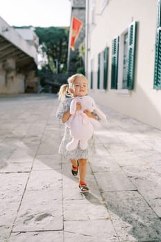 Little girl walks hugging a pink toy rabbit through the courtyard of an old castle. High quality photo