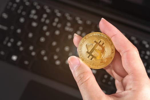 Woman hand holding golden coloured bitcoin coin over black laptop keyboard