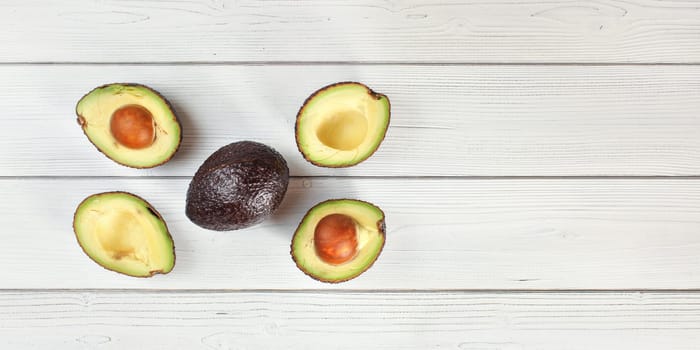 Ripe brown avocado - Hass bilse variety - halved and arranged on white boards desk, view from above, space for text right side