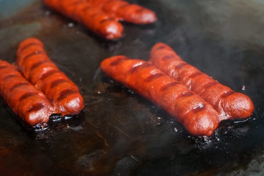 Small bratwurst / hot dog frankfurter sausages grilled on electric grill, smoke visible above