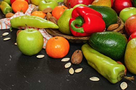 Mixed fruits and vegetables - red peppers, avocado, apples, pears, tangerines, pecan nuts, almonds and pumpkin seeds on wooden bowl, close up view from above