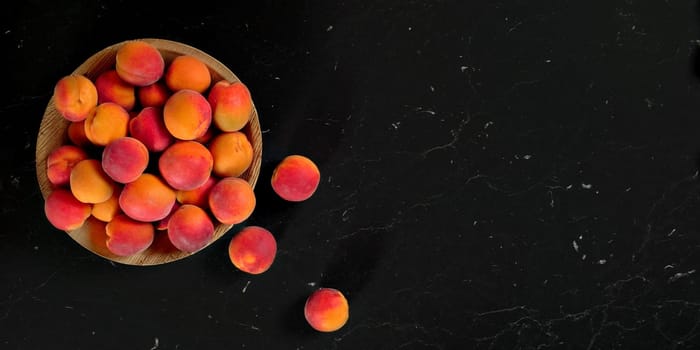 Small bowl with apricots, some of them scattered near on black marble like table - view from above, space for text right side